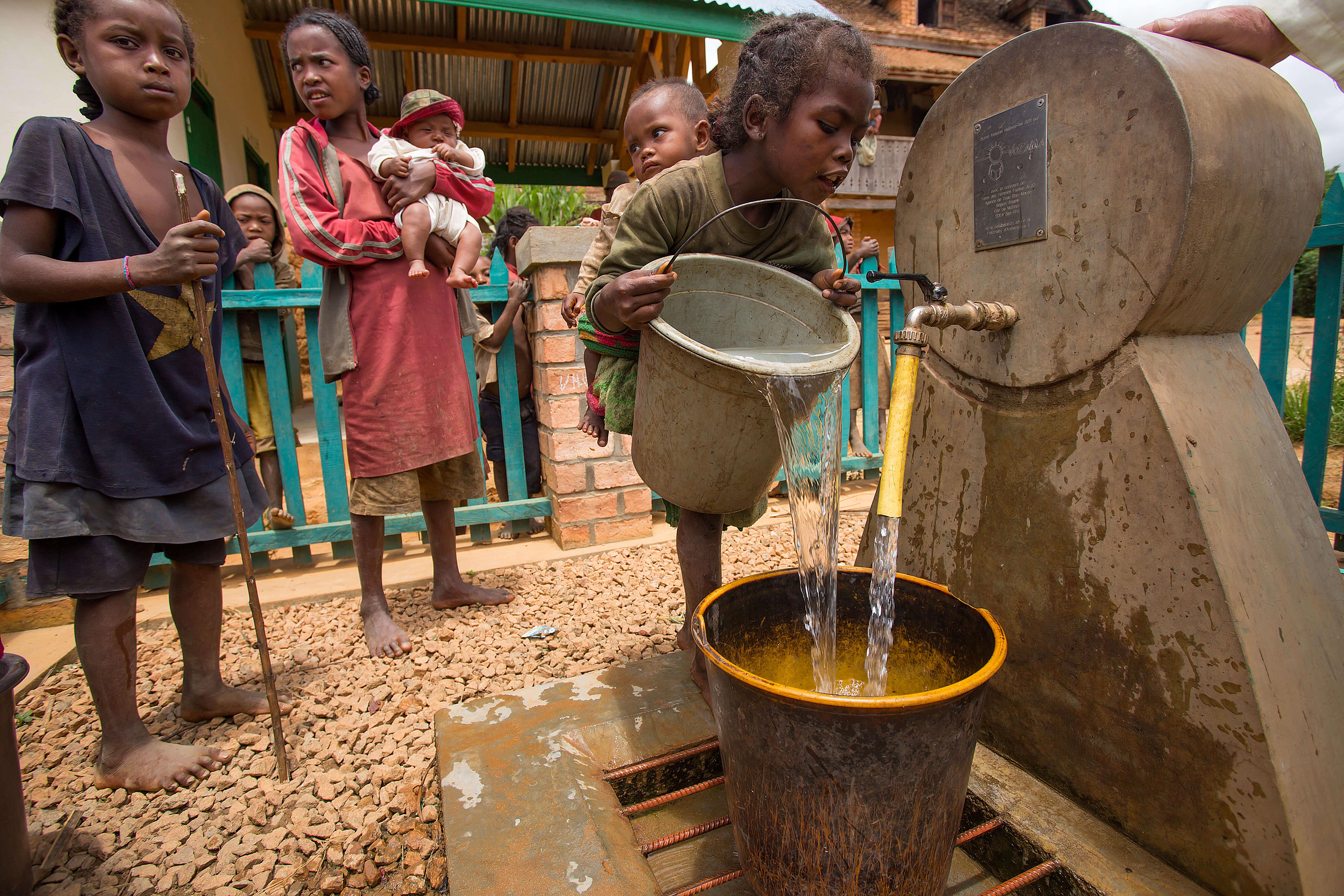 enfant versant eau dans seau borne fontaine